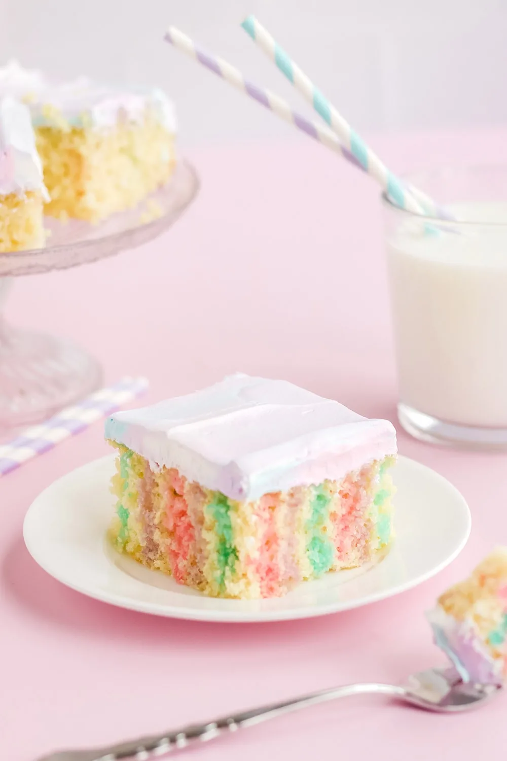 Colorful cake on a plate with milk and more cake in the background.