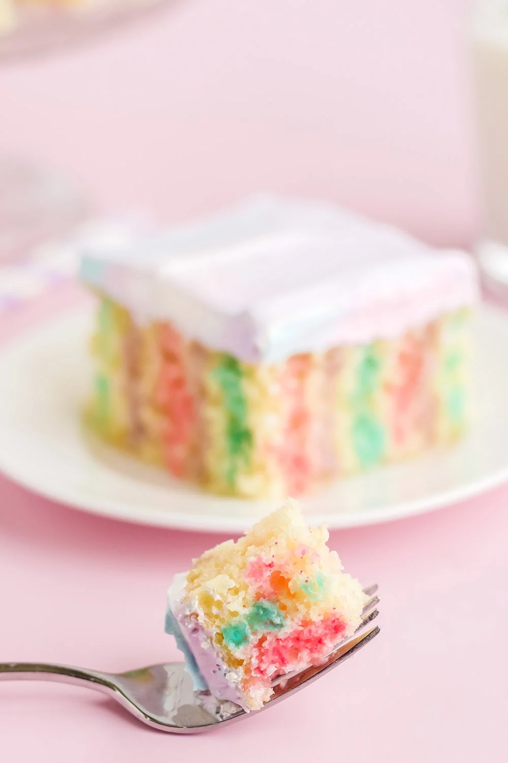 Colorful jello poke cake on a plate with a forkful in front.
