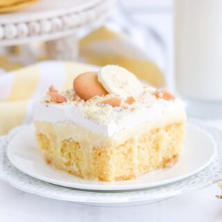 Yellow cake on a white plate on a white table with bananas and cookies.