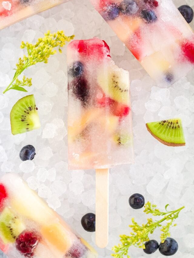 Rainbow fruit pops on ice with fresh fruit pieces.