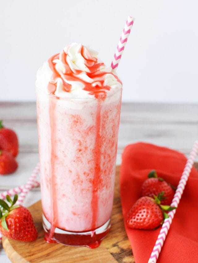 Glass of strawberry frappuccino next to strawberries.