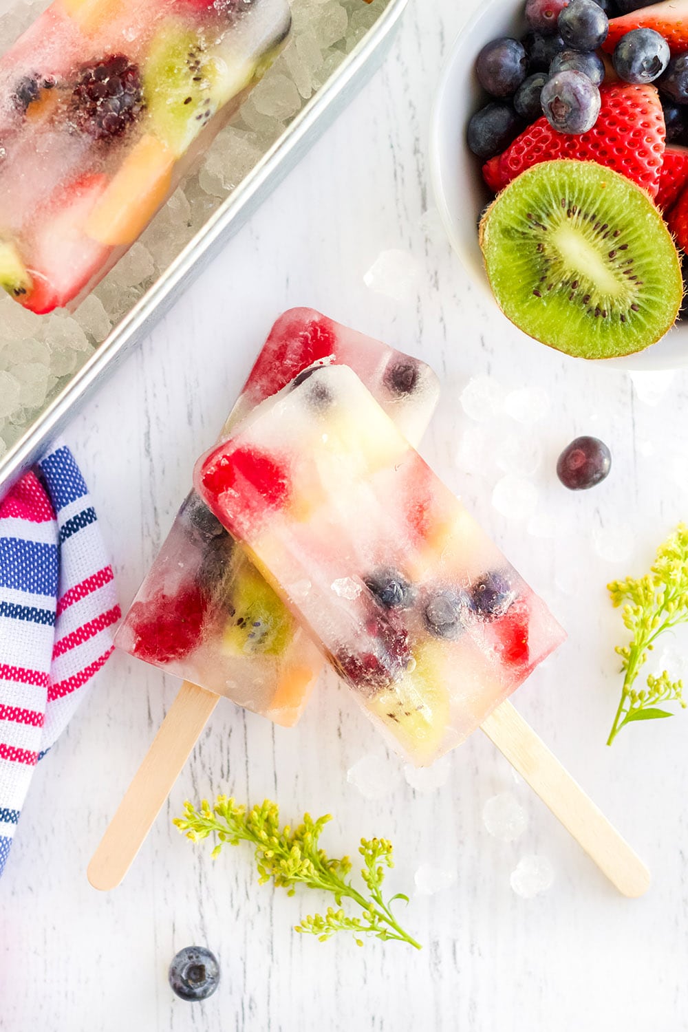 Fruit pops surrounded by fruits on a white table.