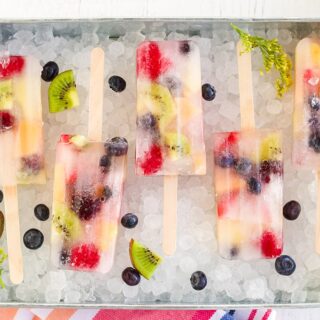 Rainbow fruit popsicles lined up in a try with nugget ice cubes.