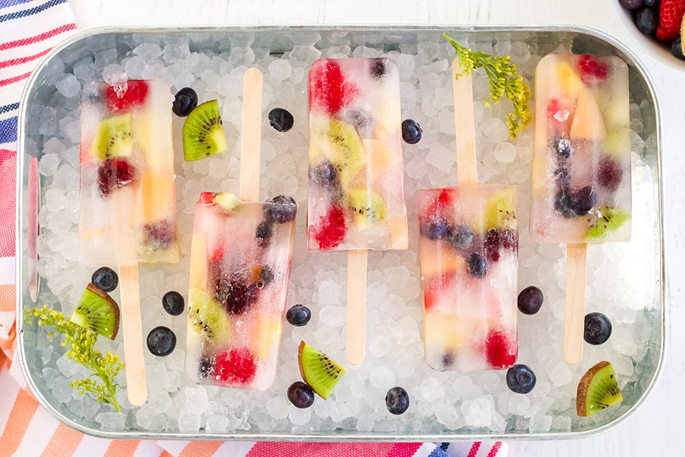 Rainbow fruit popsicles lined up in a try with nugget ice cubes.