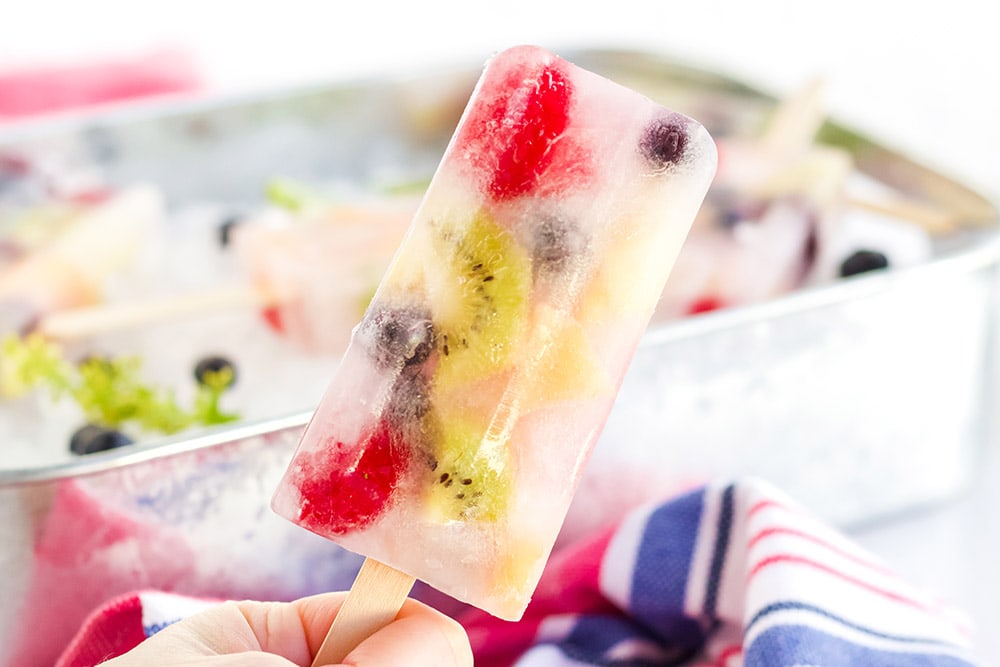 Holding a fruit popsicle with more fresh fruit pops in the background.