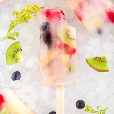 Rainbow fruit pops on ice with fresh fruit pieces.