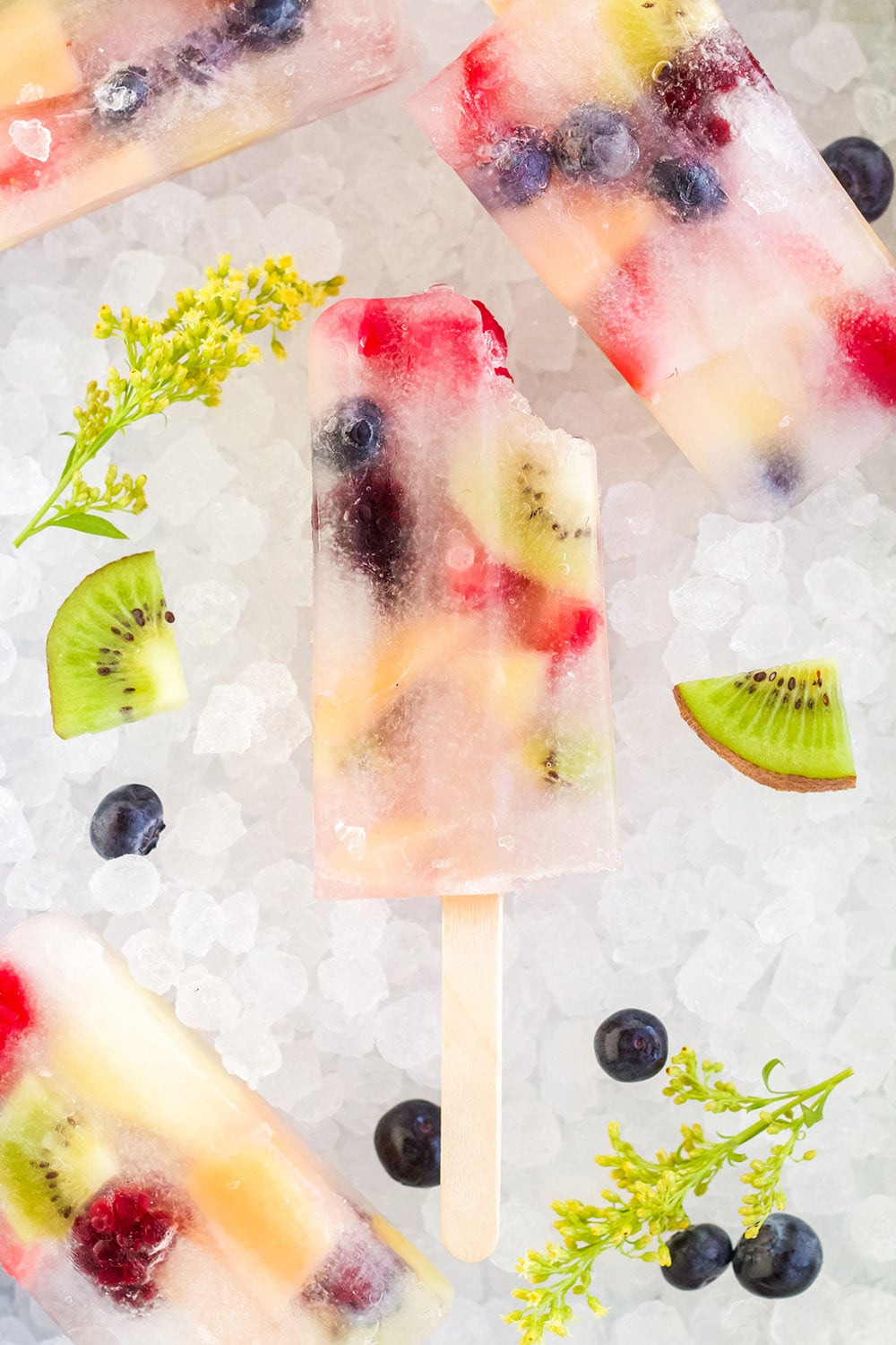 Rainbow fruit pops on ice with fresh fruit pieces.
