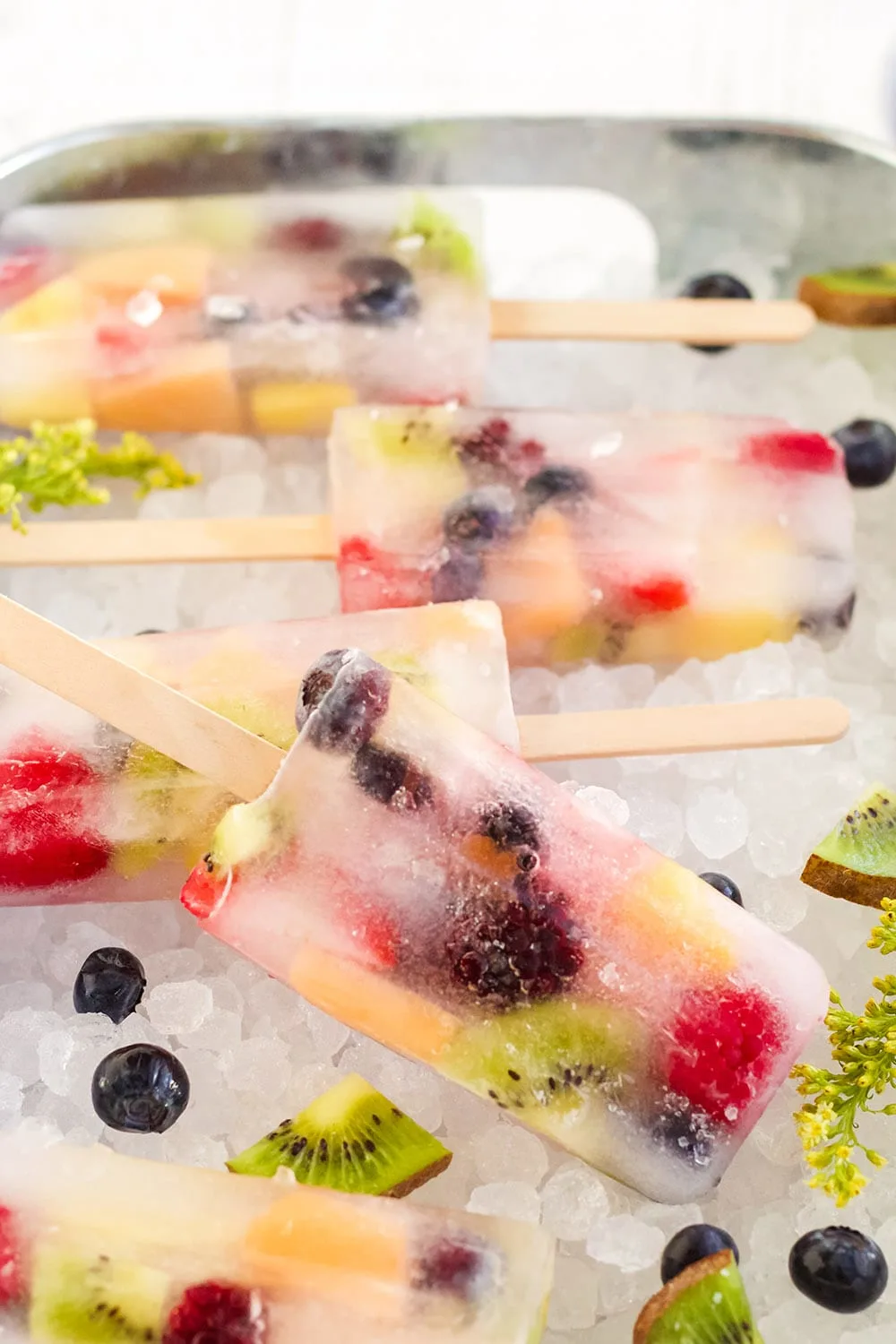 Rainbow fruit pops on a bed of ice with fruit.