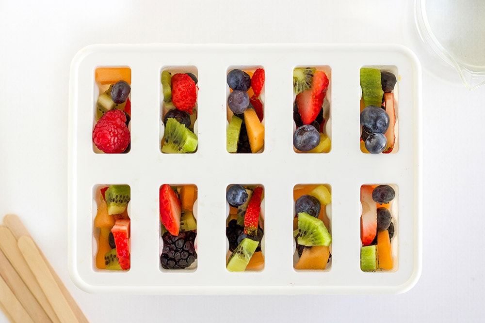 Overhead shot of fruit inside of a white popsicle mold.