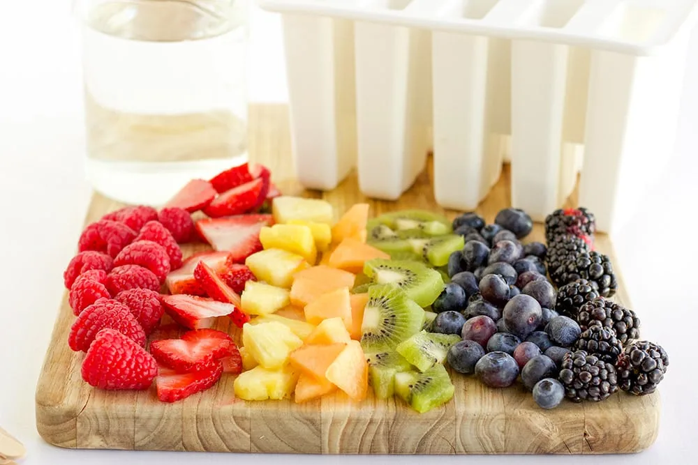 Fresh fruit on a cutting board lined up in rainbow color order. 