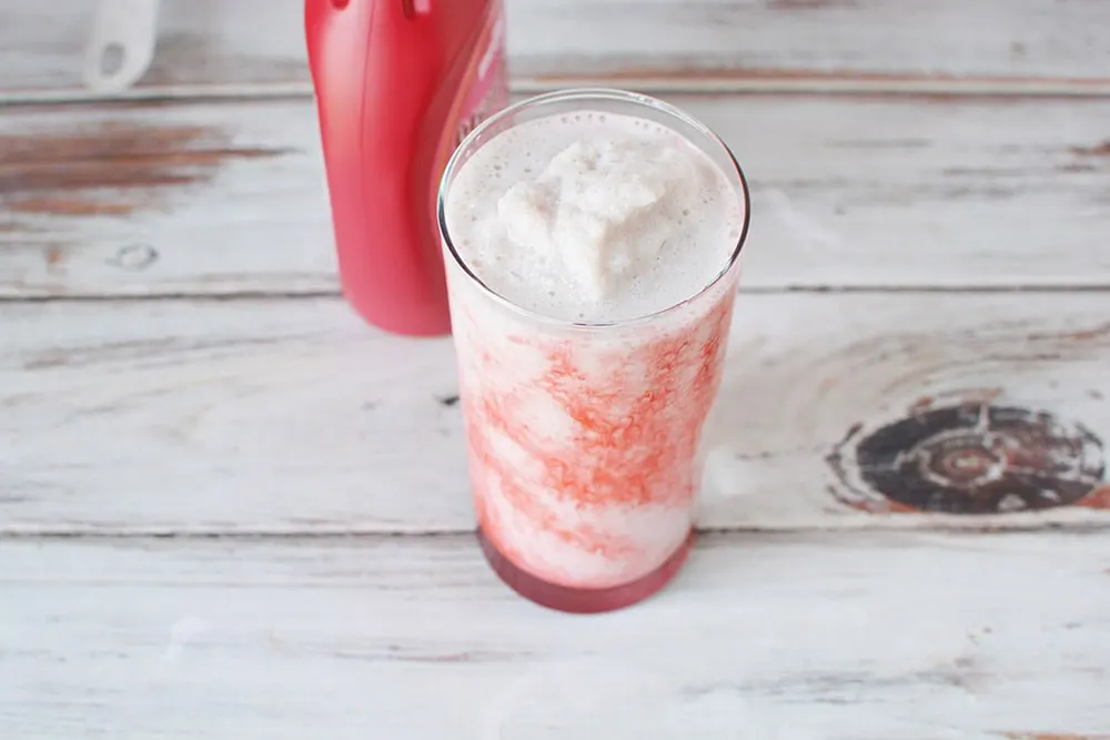 Strawberry syrup next to a glass of a pink blended drink.