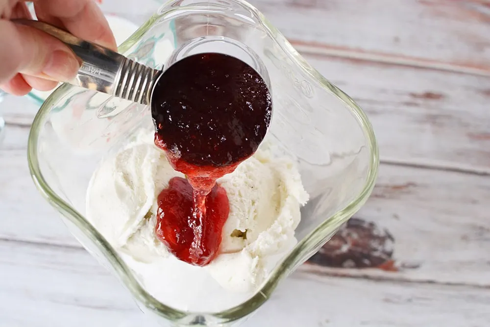 Pouring red sryup into a blender with milk and ice cream.