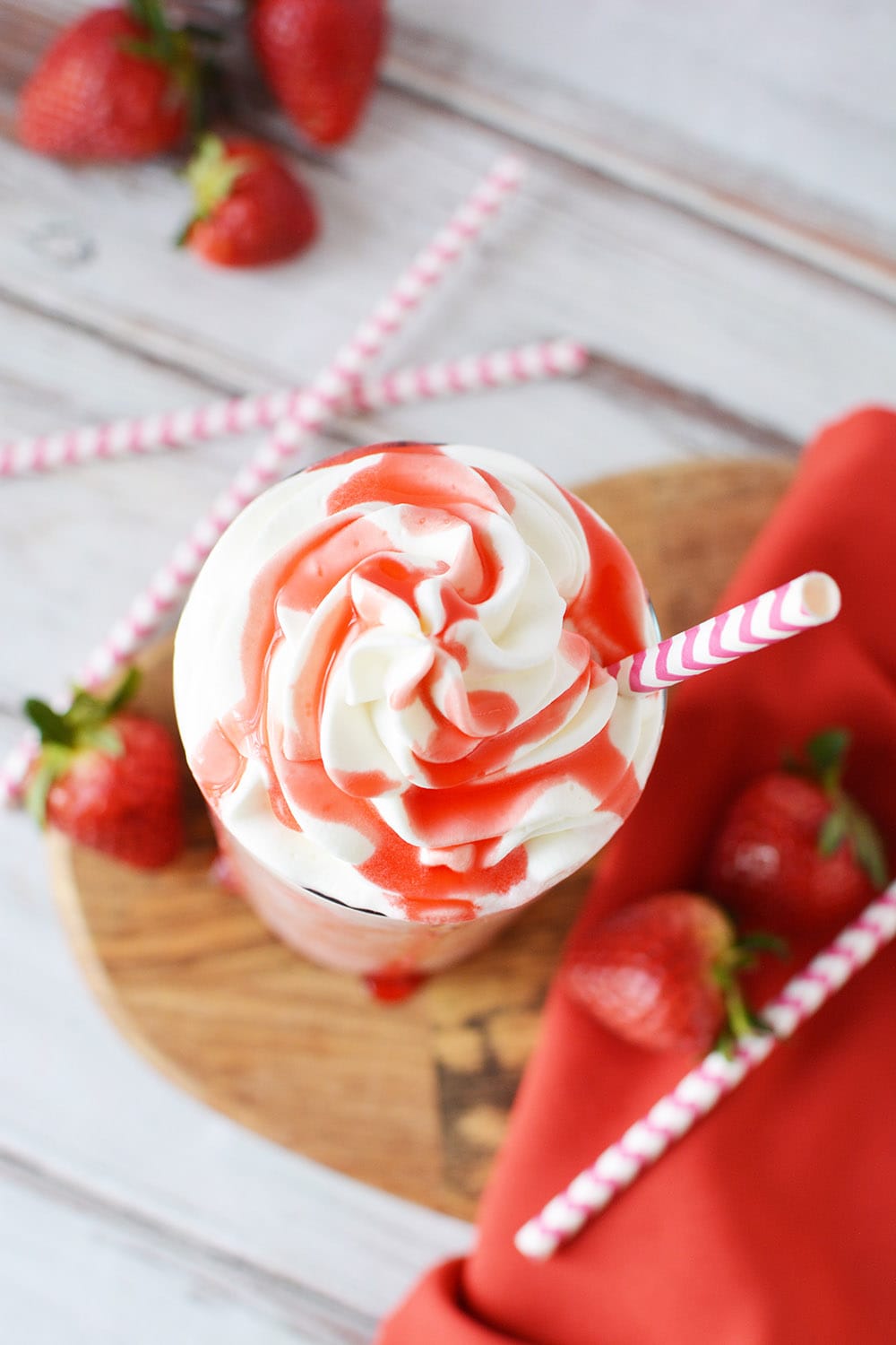 Overhead shot of strawberry syrup on top of whipped cream in a glass of a pink blended drink.