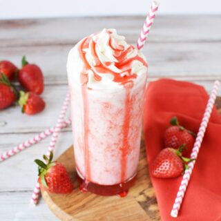 Glass of strawberry blended drink with red syrup on top of the whipped cream.