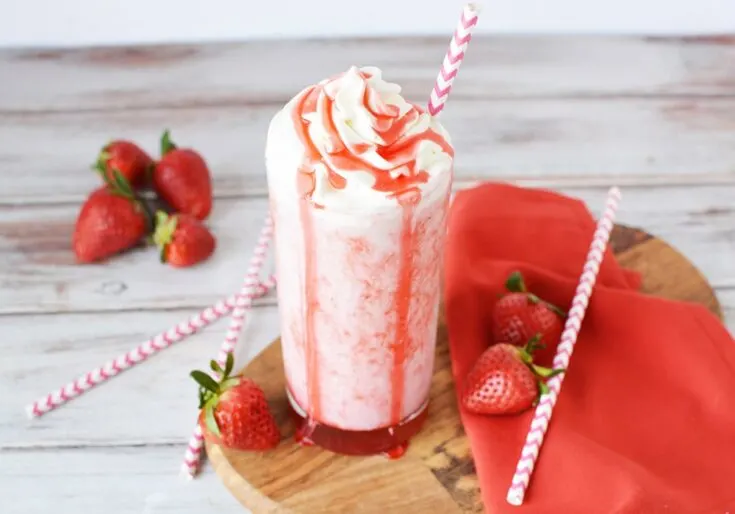 Glass of strawberry blended drink with red syrup on top of the whipped cream.