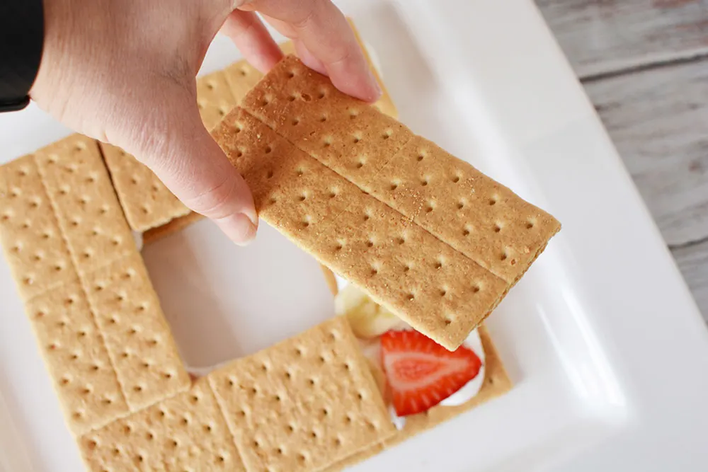 Stacking graham crackers on top of a strawberry.