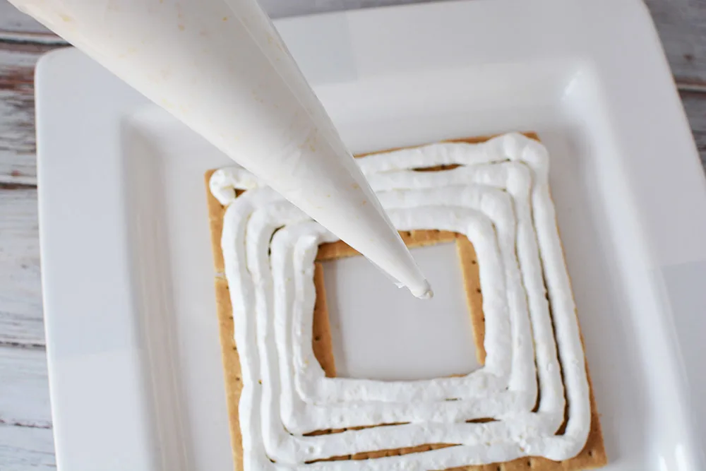 Piping whipped cream onto graham crackers.