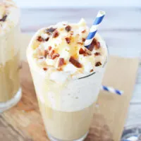 Caramel drink with whipped topping and sugar crunch with blue straw.