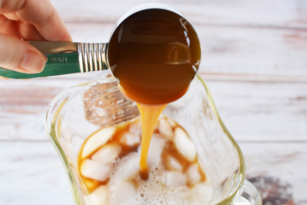Pouring caramel into a blender with ice and coffee.