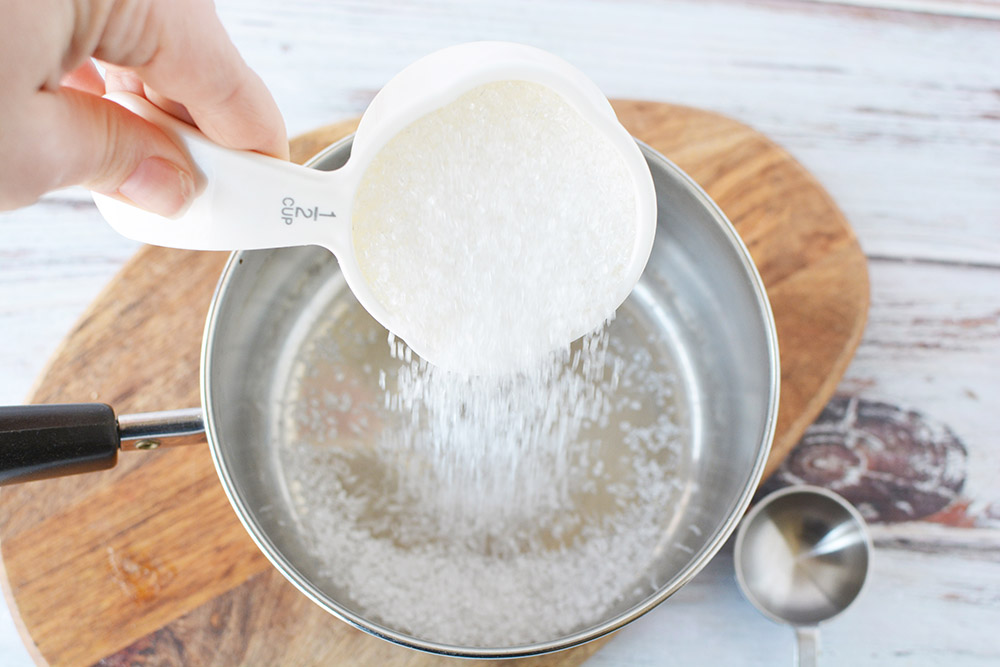 Pouring sugar into water in a sauce pan.