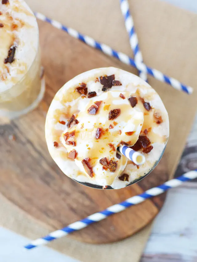 Overhead image of a caramel crunch frappuccino on a board with blue straws.