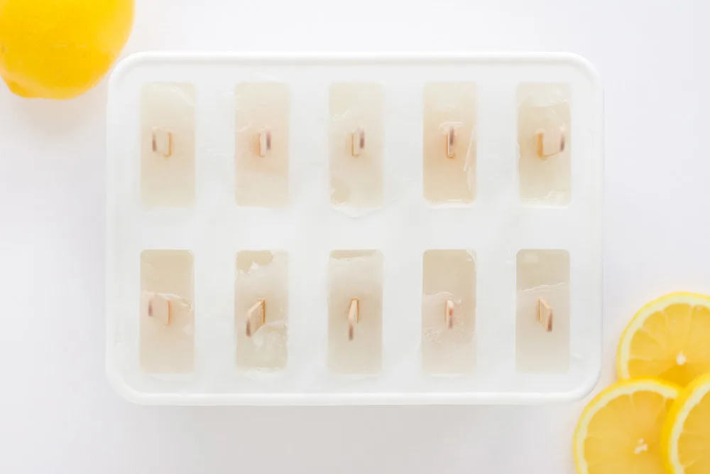 Frozen ice pops in the mold with lemon slices on the table.