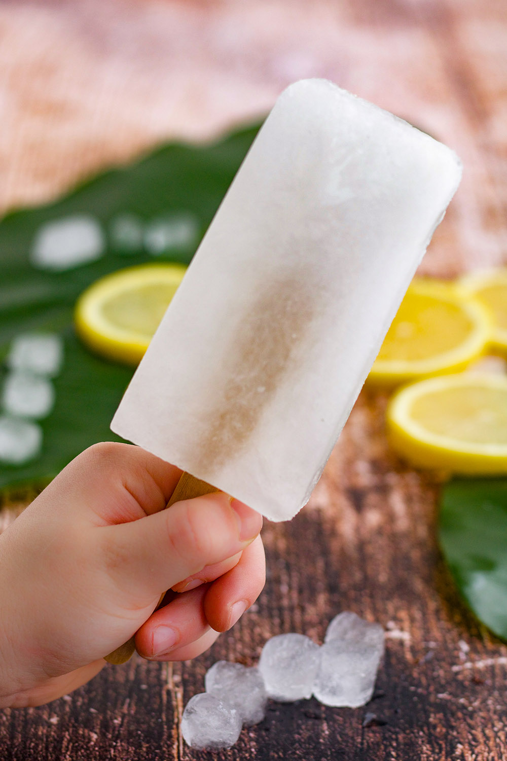 Holding a lemon ice pop with slices in the background.