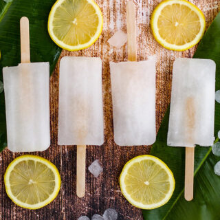 Four lemon popsicles in a row on a table with greens and lemon slices.