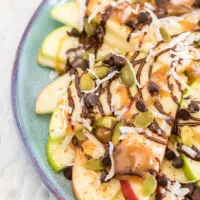 Green and red apple slices on a plate topped with, chocolate, caramel, nuts, and toppings.