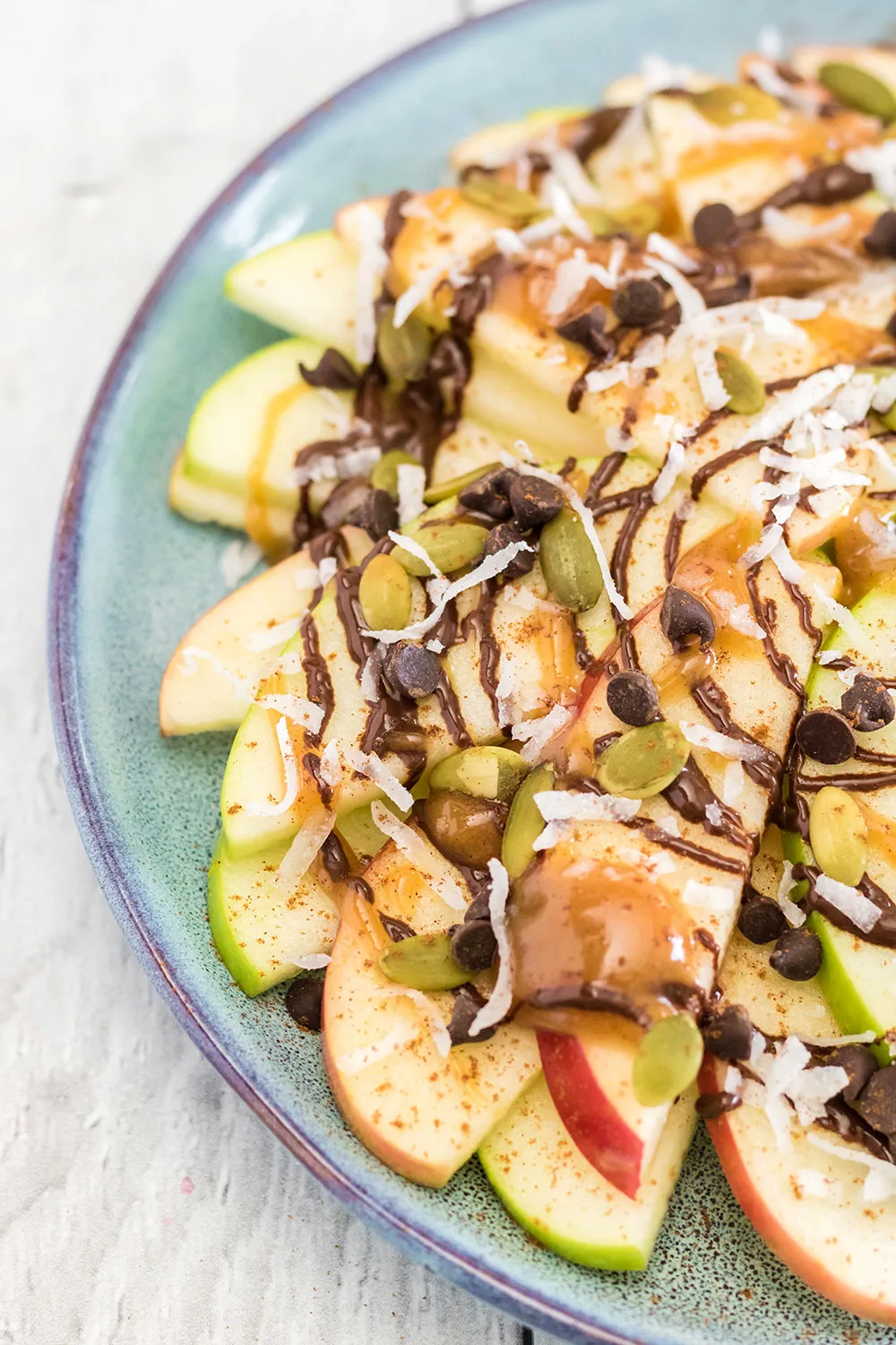 Green and red apple slices on a plate topped with, chocolate, caramel, nuts, and toppings.