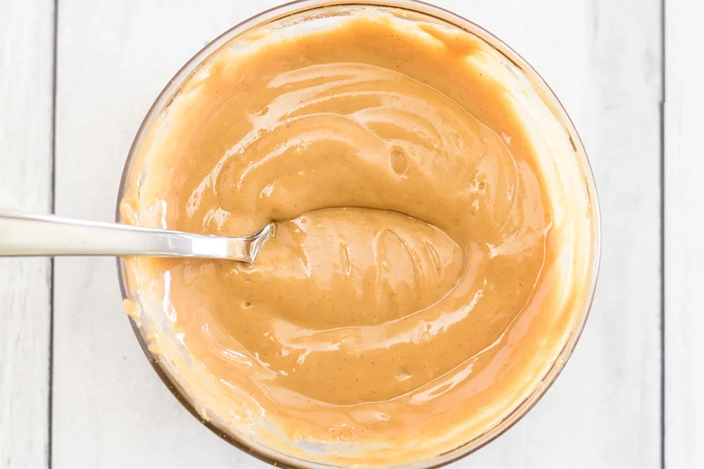 Bowl of creamy peanut butter with a spoon in it.