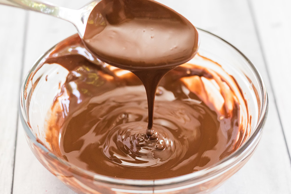 Bowl of chocolate sauce with a spoon drizzling it.