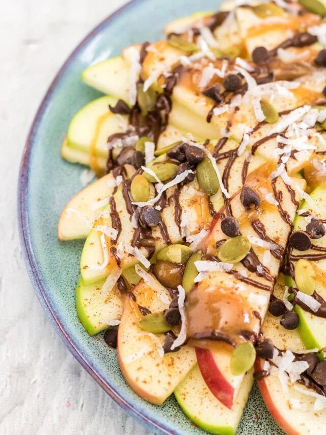 Green and red apple slices on a plate topped with, chocolate, caramel, nuts, and toppings.