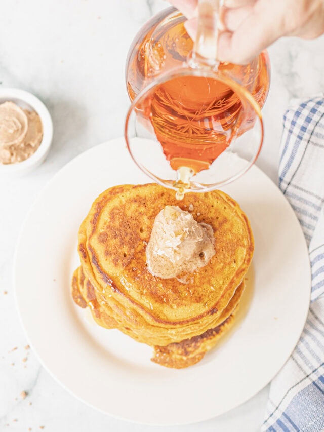 Pouring syrup over pumpkin pancakes with a scoop of cinnamon butter.