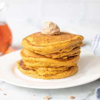 Pancakes stacked on a plate with syrup in the background.