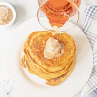 Pouring syrup over pumpkin pancakes with a scoop of cinnamon butter.