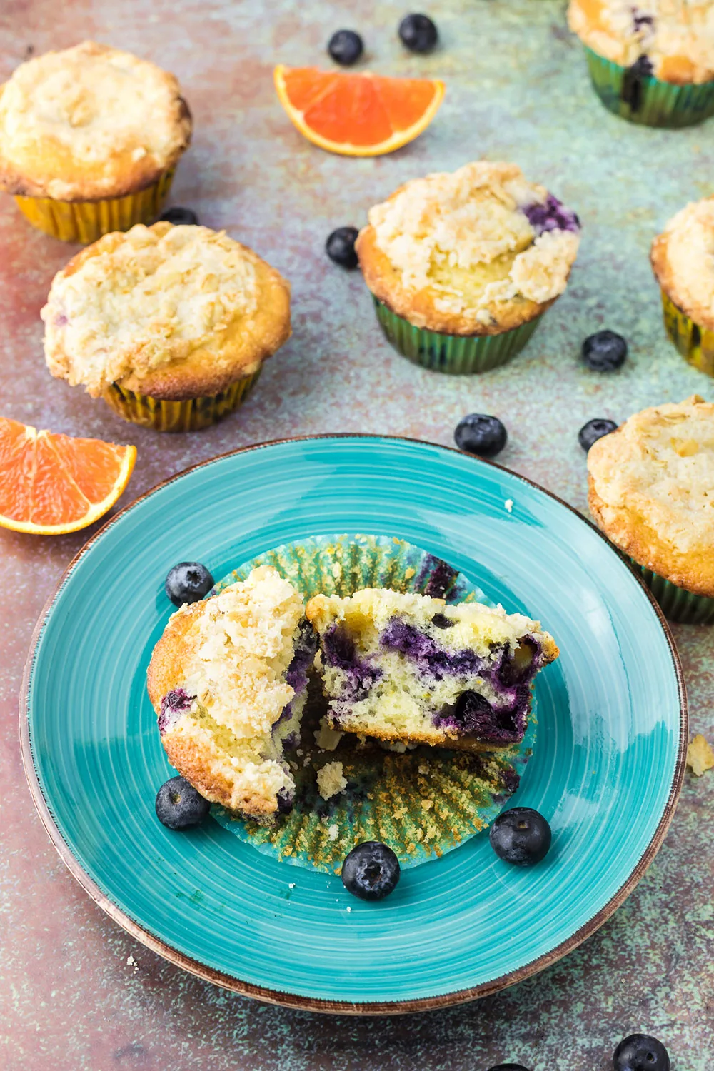 Orange blueberry muffin broken open on blue plate. More muffins around it on a table.