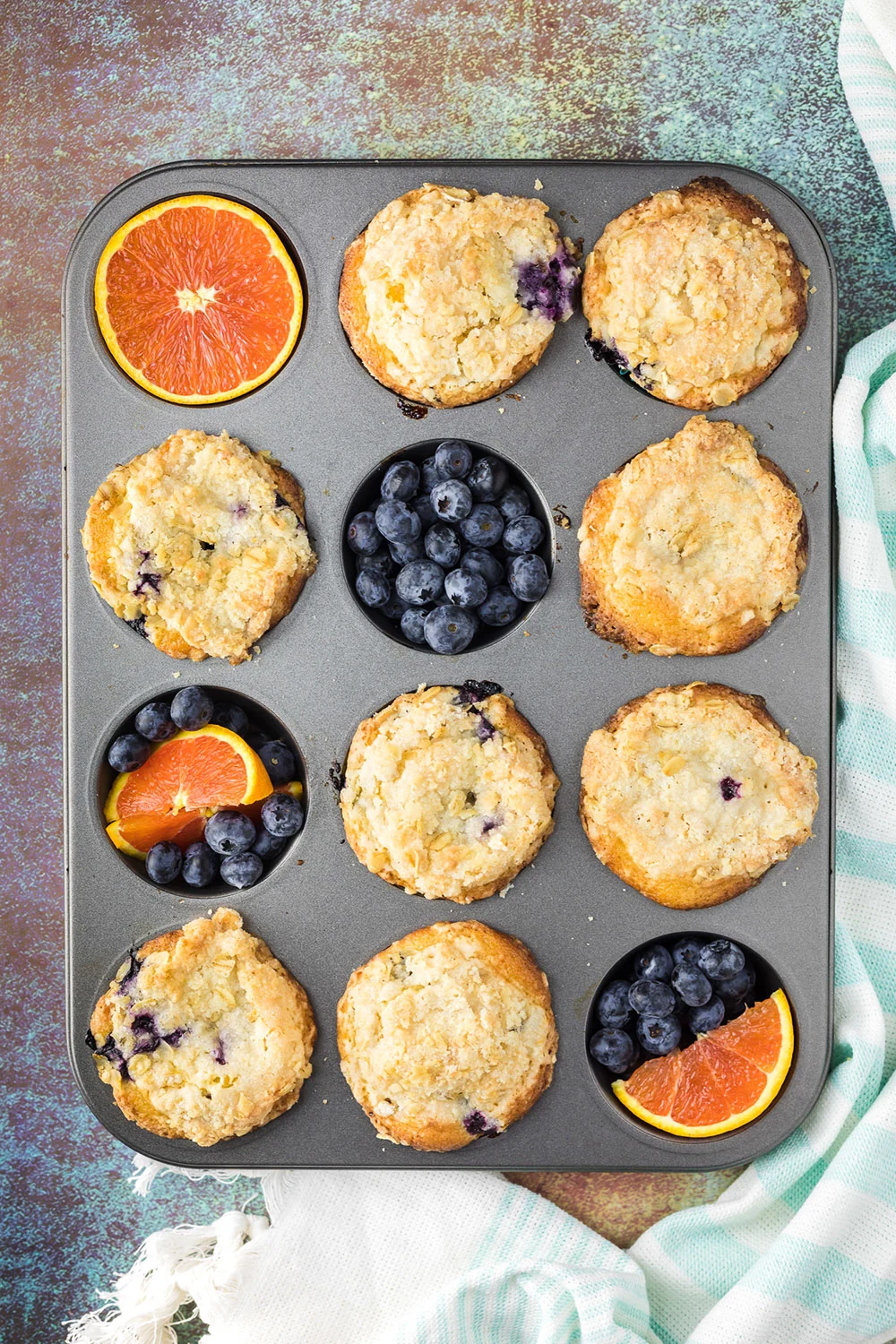 Muffin tin with muffins, oranges, and blueberries in it.