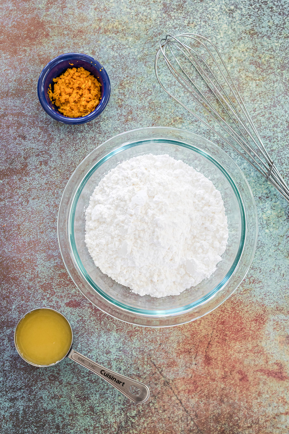 Powdered sugar, orange juice, and carrots in bowls.