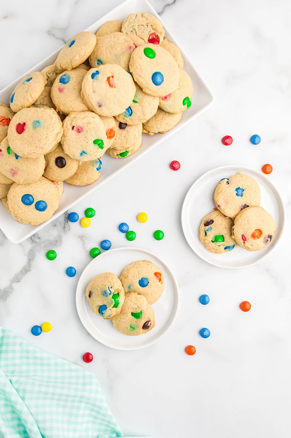 Overhead image of cookies on plates and on a tray with M&M's sprinkled on the table.