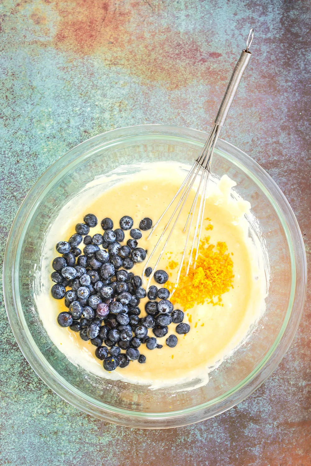 Blueberries and orange zest in muffin batter in a mixing bowl.