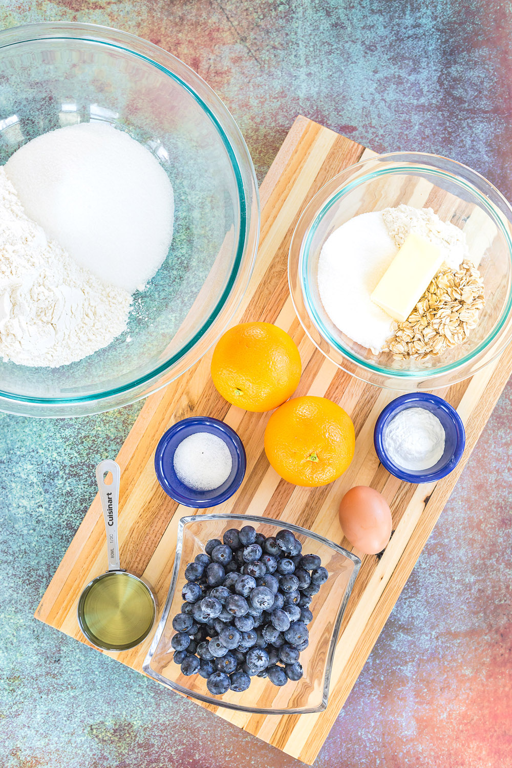 Oranges, blueberries, and other ingredients to make muffins on a board.
