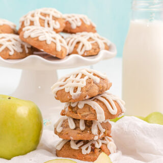 Stacked apple cookies next to a green apple and a plate of more cookies.