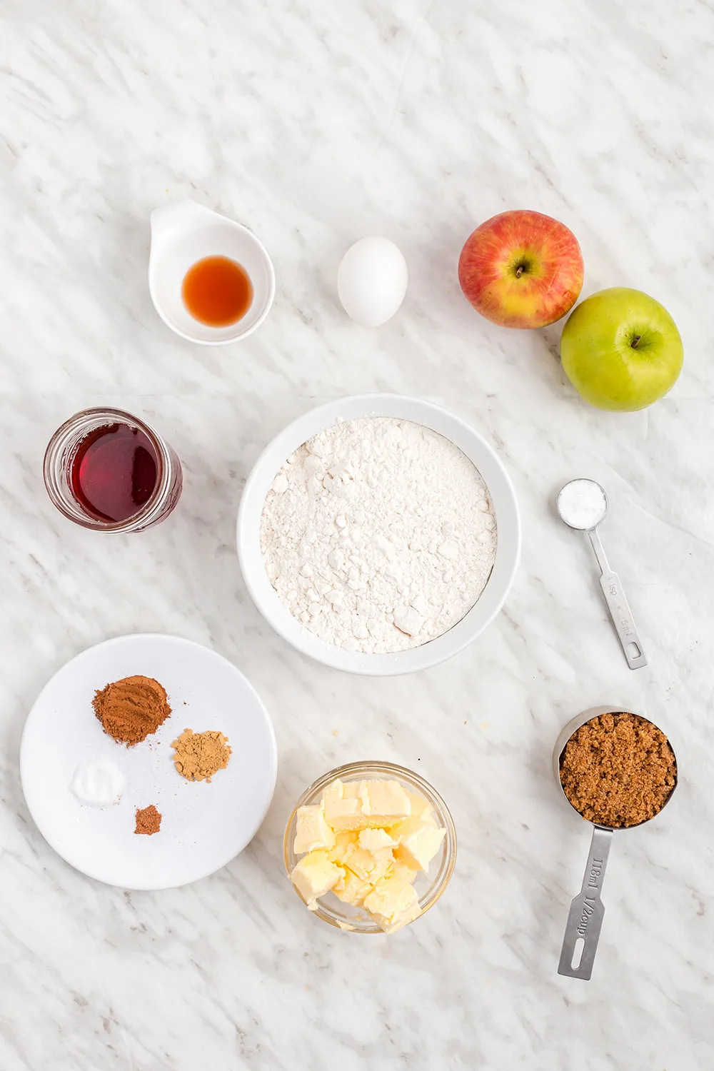 Apples, flour, cinnamon, and other ingredients on a table.