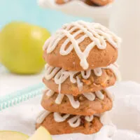 Stacked apple cookies with glaze and an apple in the background.