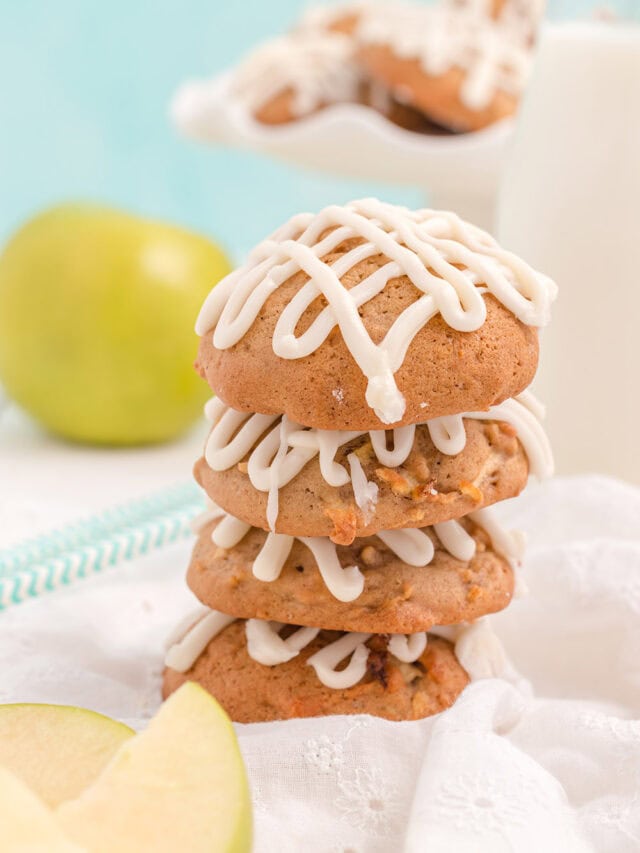 Stacked apple cookies with glaze and an apple in the background.