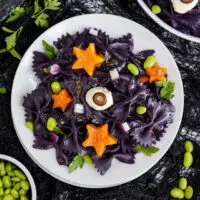 Overhead image of halloween pasta salad with bowls of ingredients on the table.
