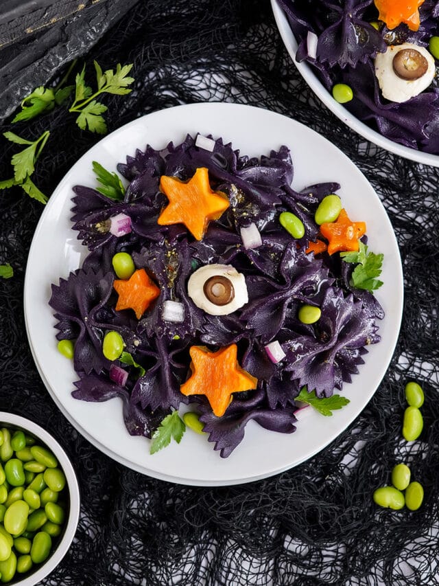 Overhead image of halloween pasta salad with bowls of ingredients on the table.