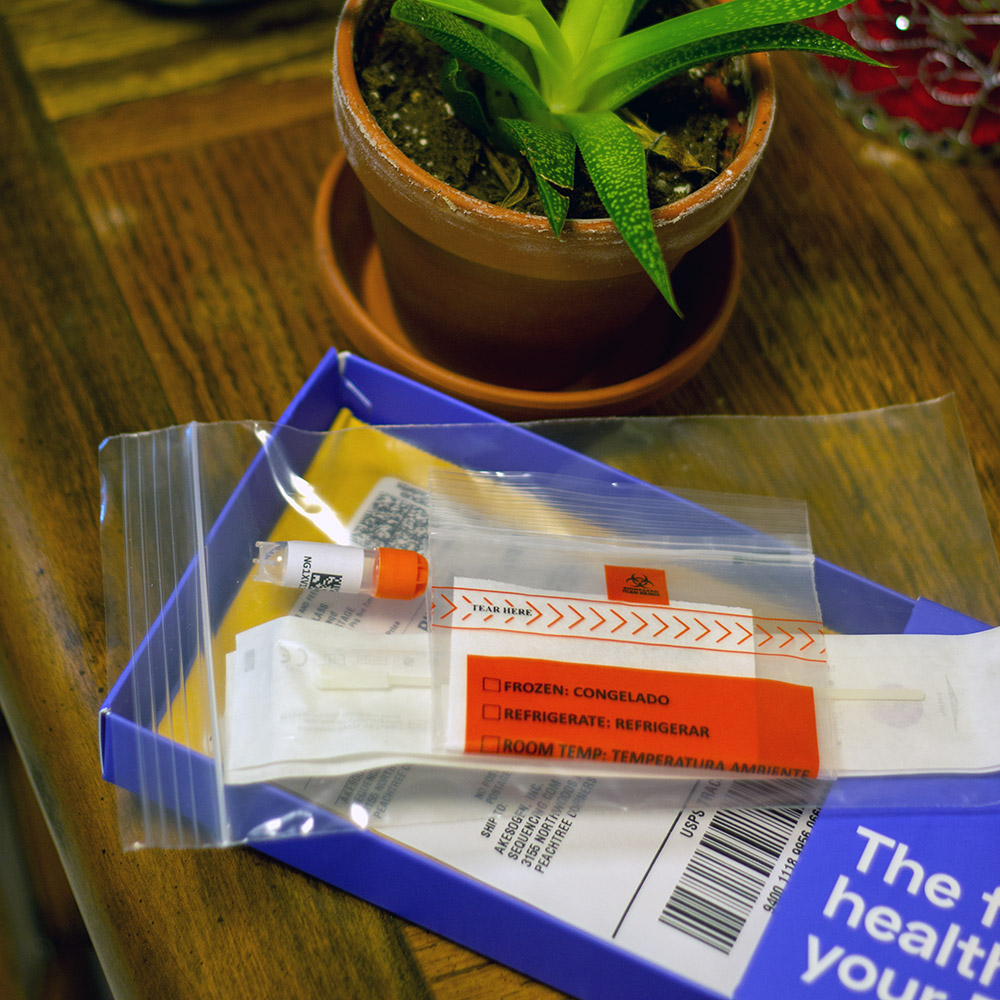 Vial and bags from the DNA test kit on a table with a plant.
