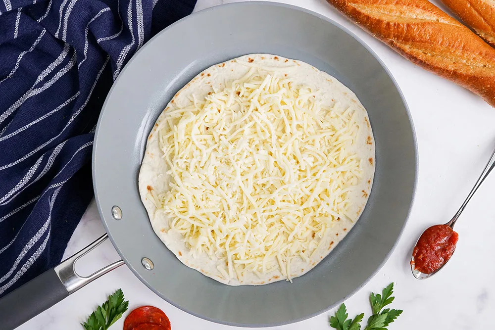 Tortilla topped with cheese in a skillet.